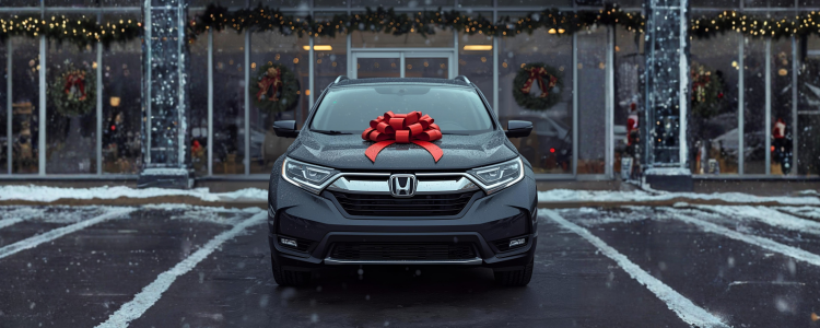 Vehicle parked at a dealership with a holiday bow on the hood and Christmas décor during winter